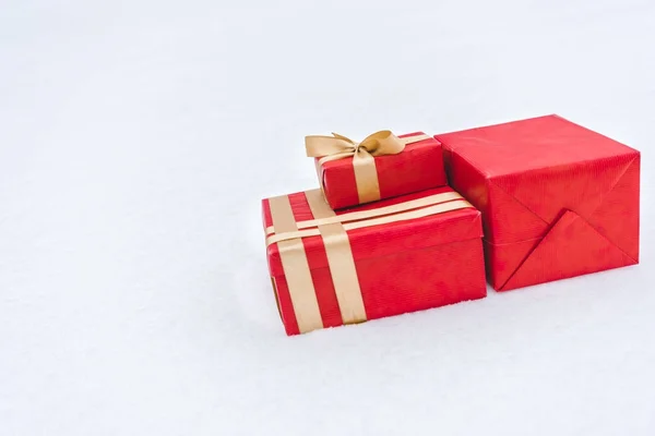 Close-up view of red gift boxes wrapped with golden ribbons on snow — Stock Photo