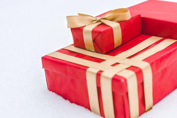 Close-up view of red gift boxes with golden ribbons in snow — Stock Photo