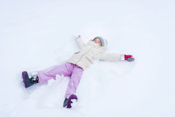 Cute little child in warm clothes making snow angle — Stock Photo