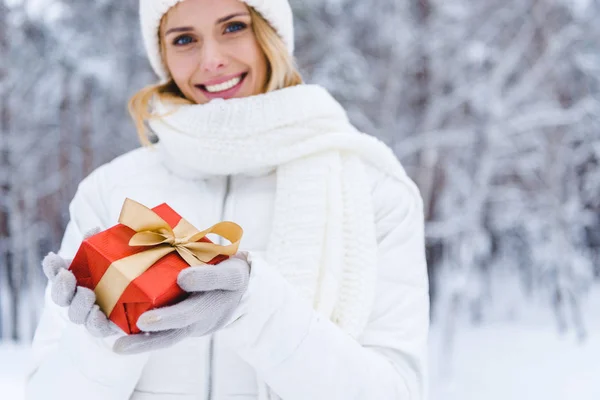 Donna felice che tiene la scatola regalo e sorride alla macchina fotografica nel parco invernale — Foto stock