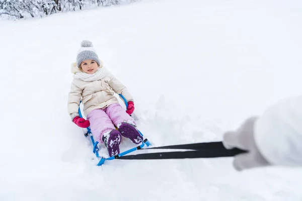 Recortado disparo de la madre llevando lindo niño sentado en trineo en el parque de invierno - foto de stock