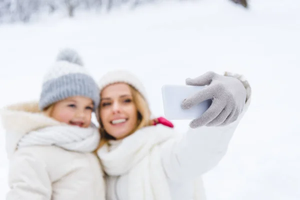 Selective focus of happy mother and daughter taking selfie with smartphone in winter park — Stock Photo
