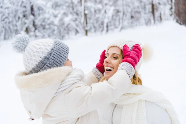 Schöne glückliche Mutter und Tochter tragen Hüte und lächeln einander im Winterpark zu — Stockfoto