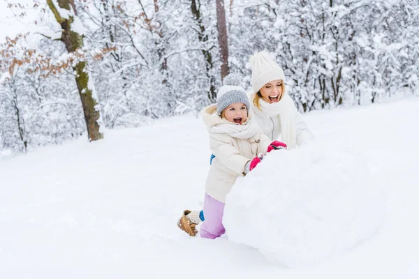 Feliz madre y linda hijita haciendo muñeco de nieve juntos en el parque de invierno - foto de stock