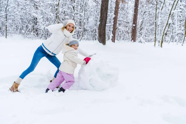 Mère et fille heureux faisant bonhomme de neige et souriant à la caméra dans le parc d'hiver — Photo de stock