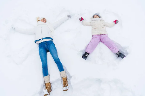Vue en angle élevé de mère et fille heureuses faisant anges de neige et se souriant — Photo de stock