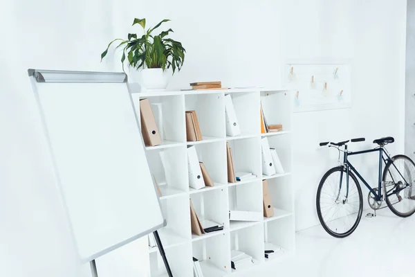 Lavagna a fogli mobili con bicicletta e ripiani in legno in ufficio vuoto — Foto stock