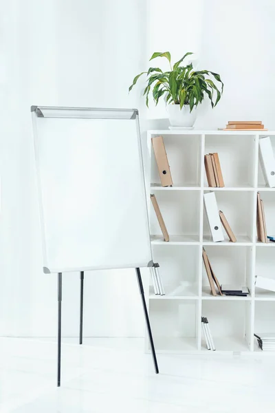 Empty flipchart and wooden shelves with folders in office — Stock Photo