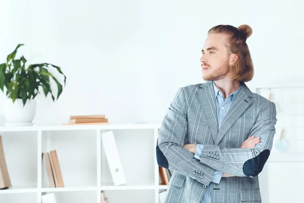 Bel homme d'affaires debout dans le bureau avec les bras croisés et détournant les yeux — Photo de stock