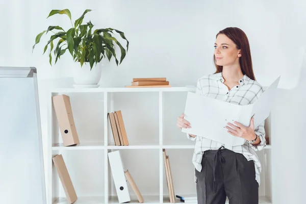 Atractiva mujer de negocios sosteniendo carpeta y mirando hacia otro lado - foto de stock