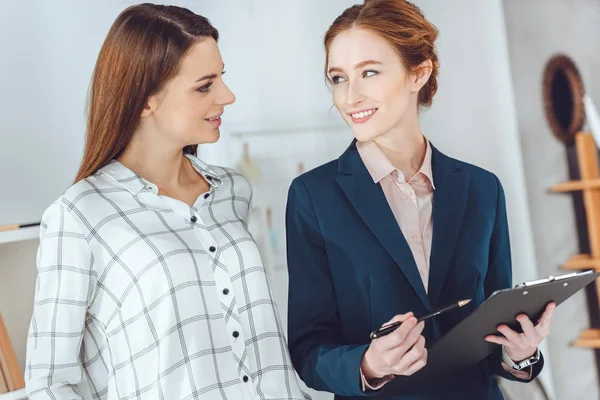 Lächelnde Geschäftsfrauen, die im Büro reden und einander anschauen — Stockfoto