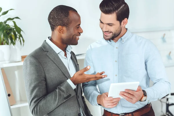 Sorridenti uomini d'affari afro-americani e caucasici che parlano in ufficio e usano tablet — Foto stock