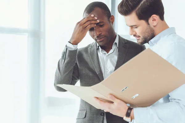 Hommes d'affaires afro-américains et caucasiens à la recherche de documents dans le dossier — Photo de stock