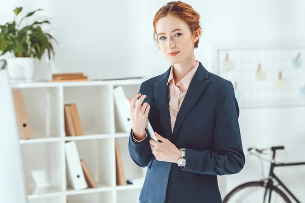 Smiling businesswoman holding tablet and looking at camera — Stock Photo