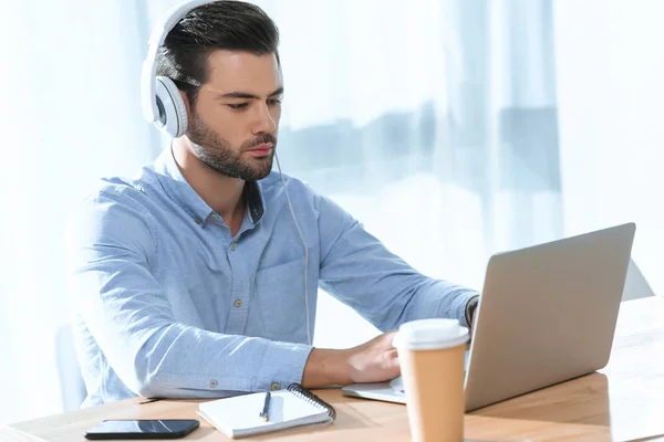 Handsome businessman listening music and working at laptop — Stock Photo