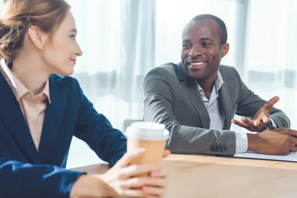 Homem africano sorrindo para a mulher com café nas mãos no espaço de escritório — Fotografia de Stock