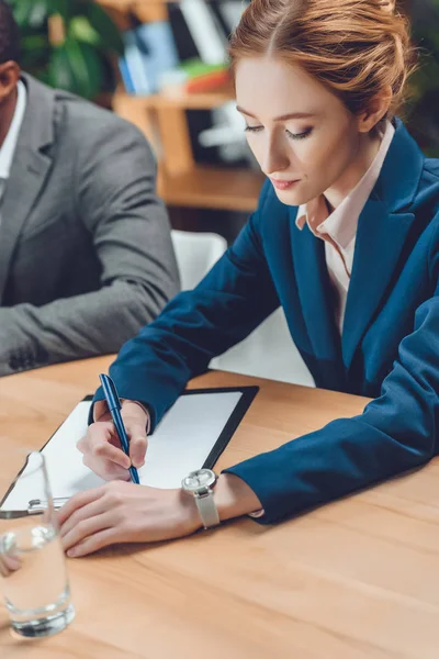 Geschäftsfrau schreibt auf Papier in Mappe auf Tisch im Büro — Stockfoto