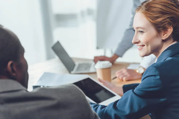 Mujer con tableta difital en las manos sonriendo al hombre africano sentado - foto de stock