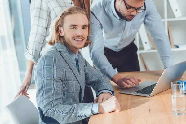 Mann lächelt in die Kamera, während andere auf Laptop auf Tisch schauen — Stockfoto