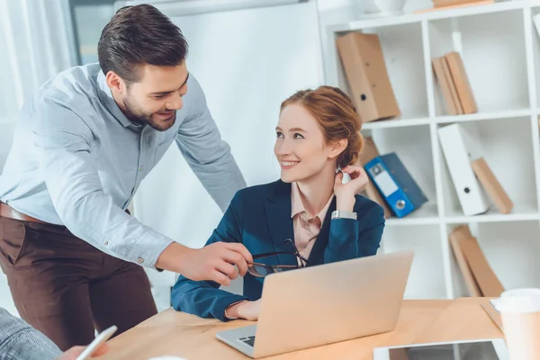 Homme debout en chemise bleue parlant à la femme assise contre ordinateur portable sur la table — Photo de stock