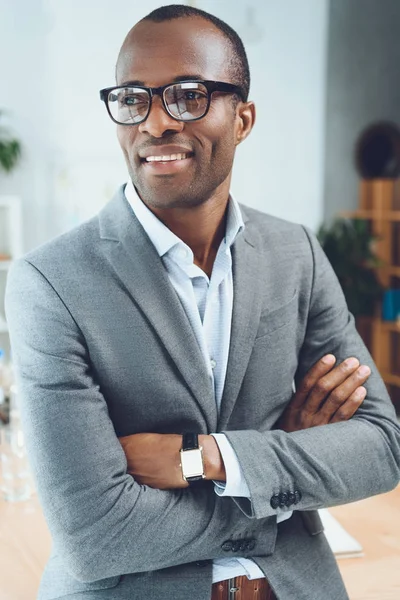 Uomo africano sorridente con le braccia incrociate guardando lo spazio ufficio — Foto stock