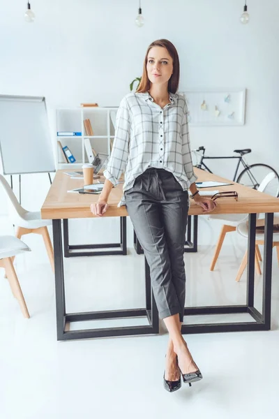 Donna in camicia appoggiata sul tavolo e guardando da un'altra parte lo spazio ufficio — Foto stock