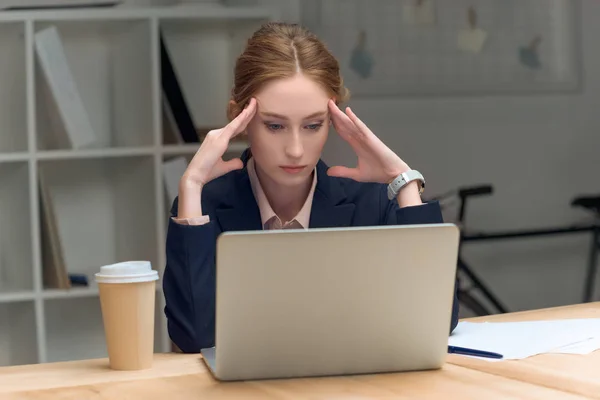 Nachdenkliche Frau sitzt am Tisch gegen Laptop und Kaffee im Becher — Stockfoto