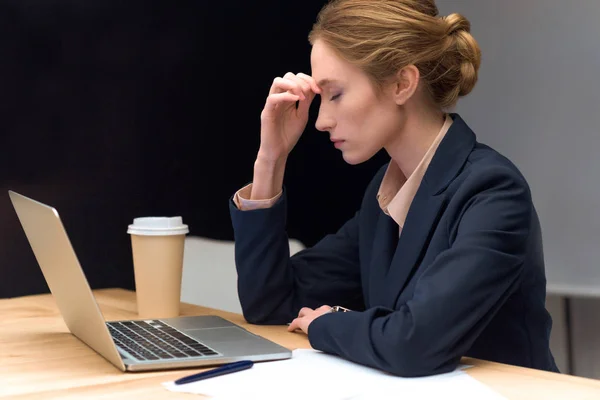 Задумчивая женщина с закрытыми глазами сидит за столом против ноутбука — стоковое фото