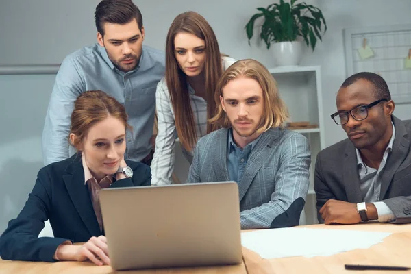 Business team sitting at table and looking on laptop — Stock Photo