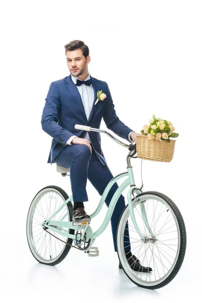 Marié en costume assis sur vélo rétro avec bouquet de mariage dans le panier isolé sur blanc — Photo de stock