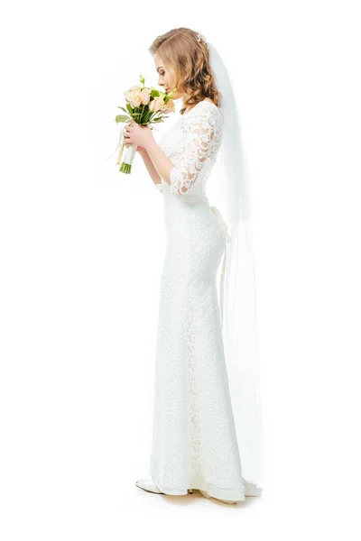 Вид збоку привабливої нареченої у весільній сукні та завісі з букетом квітів ізольовані на білому — стокове фото