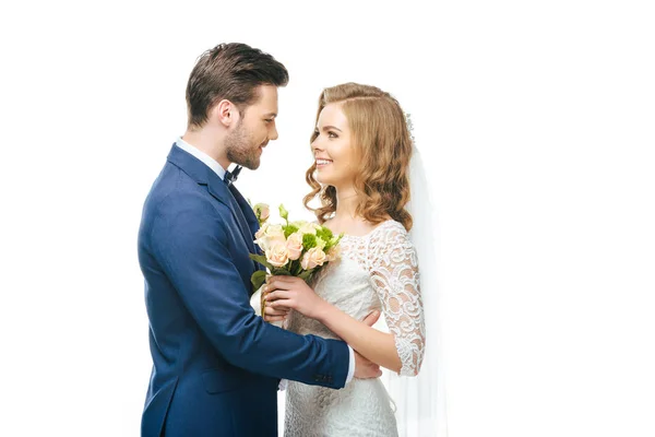 Vista lateral de la joven pareja de boda mirándose aislados en blanco - foto de stock