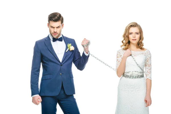 Sposo tenendo scioccato giovane sposa sulla catena isolato su bianco — Foto stock