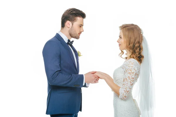 Vista lateral de la hermosa pareja de boda tomados de la mano y mirándose unos a otros aislados en blanco - foto de stock