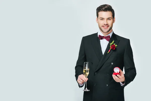 Retrato de novio sonriente con copa de champán y anillo de bodas aislado en gris - foto de stock