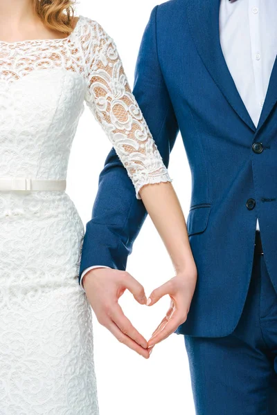 Vista parcial de la pareja de boda que muestra el símbolo del corazón hecho de manos juntas aisladas en blanco - foto de stock