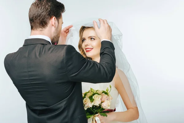 Vista parcial del novio mirando hermosa novia en velo con ramo de flores - foto de stock