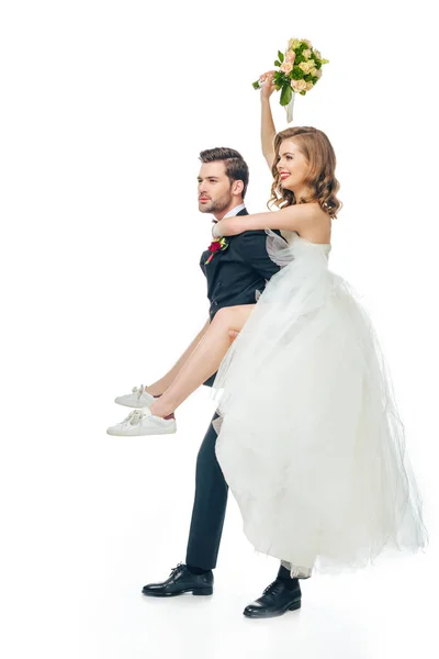 Side view of happy bride and groom piggybacking together isolated on white — Stock Photo