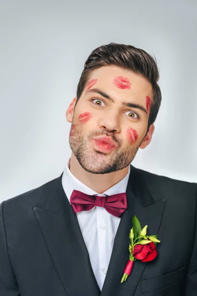 Retrato de novio guapo en traje con lápiz labial rojo en la cara aislado en gris - foto de stock