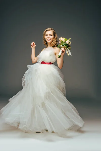 Улыбающаяся невеста в красивом свадебном платье с цветами в руке — стоковое фото