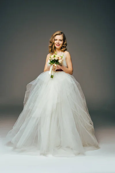 Усміхнена наречена в красивій весільній сукні з квітами в руці — стокове фото