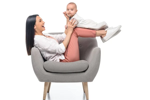 Smiling young mother resting on arm chair together with little baby isolated on white — Stock Photo