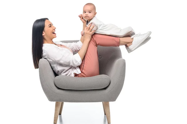 Sonriente joven madre descansando en el sillón junto con el pequeño bebé aislado en blanco - foto de stock