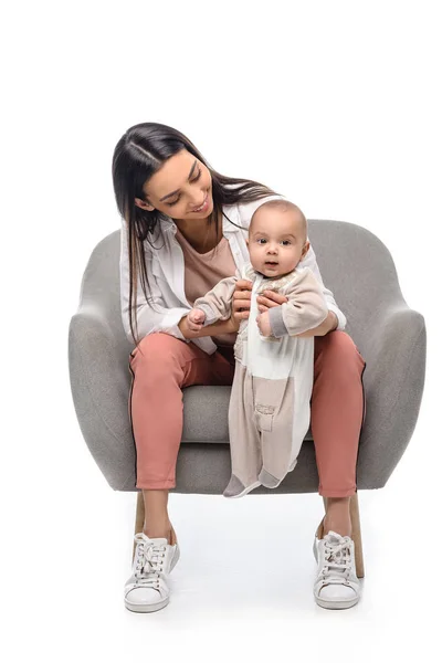 Sorridente giovane madre appoggiata sulla poltrona insieme al piccolo bambino isolato sul bianco — Foto stock