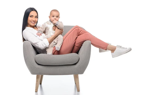 Sorridente giovane madre appoggiata sulla poltrona insieme al piccolo bambino isolato sul bianco — Foto stock