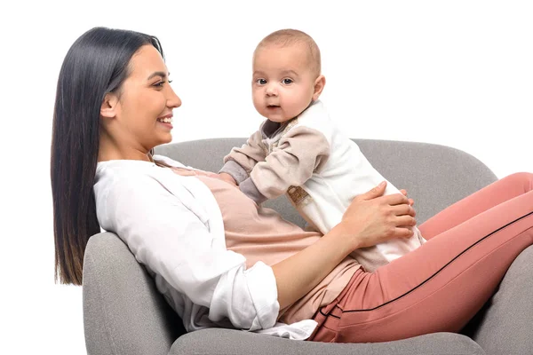 Sorridente giovane madre appoggiata sulla poltrona insieme al piccolo bambino isolato sul bianco — Foto stock