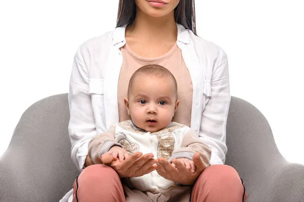 Tiro recortado de mujer sosteniendo bebé bebé mientras está sentado en silla de brazo aislado en blanco - foto de stock