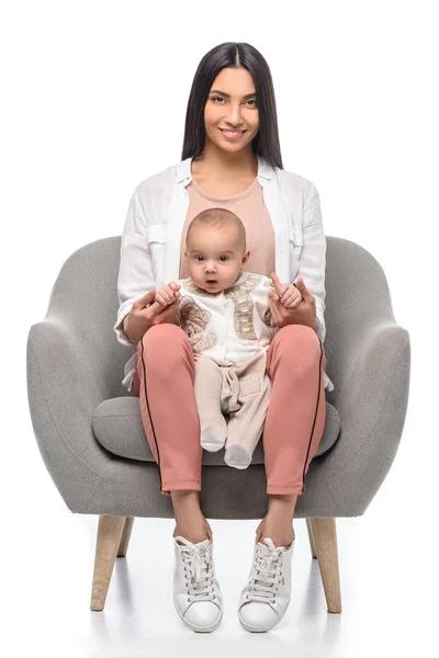 Sonriente joven madre sentada en el sillón junto con un pequeño bebé aislado en blanco - foto de stock