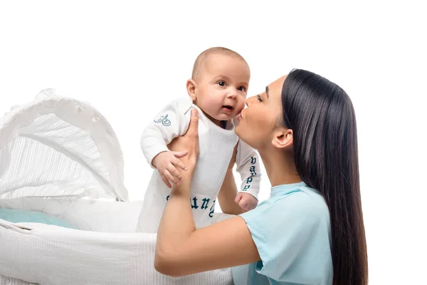 Vista lateral da mãe beijando bebê bebê no berço isolado no branco — Fotografia de Stock