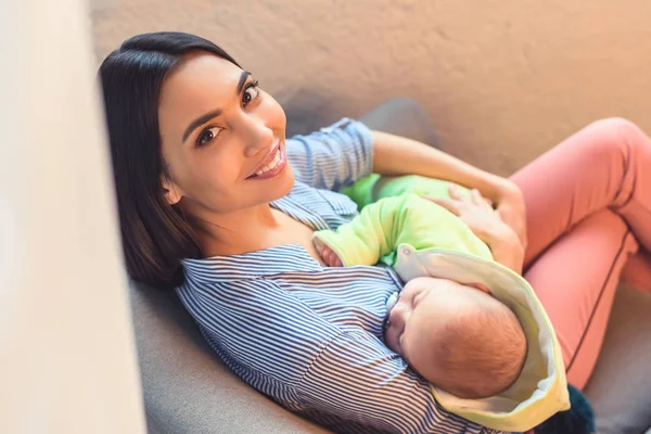 Vista lateral de la madre sonriente con bebé bebé descansando en el sillón del brazo en casa - foto de stock